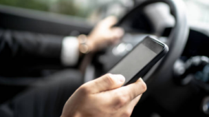 Homem ao volante consultando um telefone celular